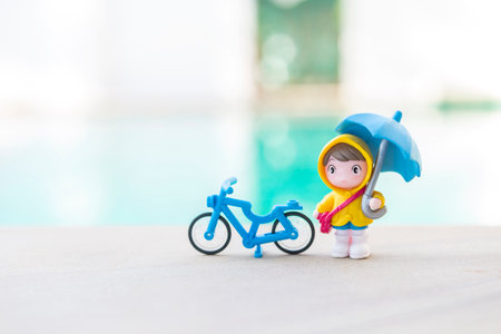Miniature boy in yellow rain coat holding umbrella with blue bicycle over blurred background, outdoor day lightの写真素材