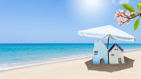 Miniature house under white beach umbrella on tropical beach background, property and real estate business concept, summer house, outdoor day lightの写真素材