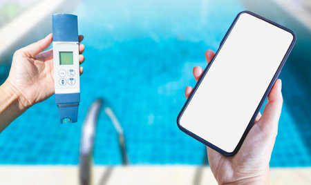 Digital water tester and smartphone in girl hand over blurred swimming pool background, online water quality check serviceの写真素材