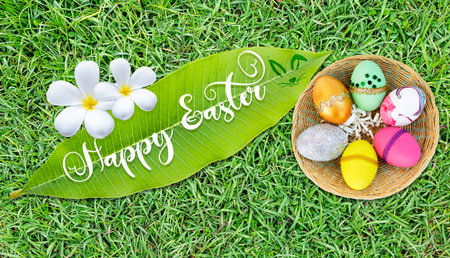 Happy Easter sign on green leaf with colourful egg in wood basket on fresh green grass background, Easter greeting card background ideaの写真素材