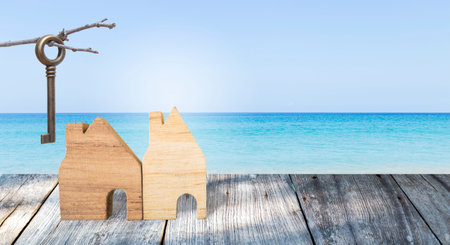 Wooden house model with old key over tropical beach background, property and real estate business concept, summer houseの写真素材