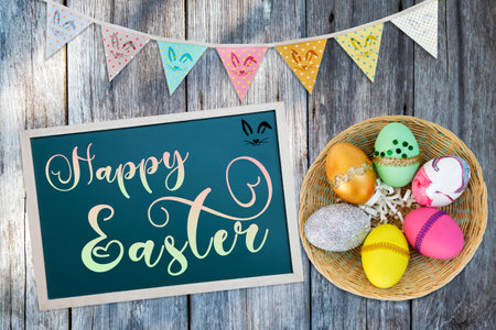 Happy Easter greeting card background idea, sign with colourful easter egg and bunting flag on wood backgroundの写真素材