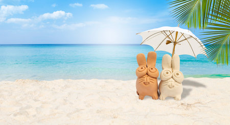 Cute little rabbit clay sculpture with white beach umbrella on tropical beach background, summer outdoor day lightの写真素材