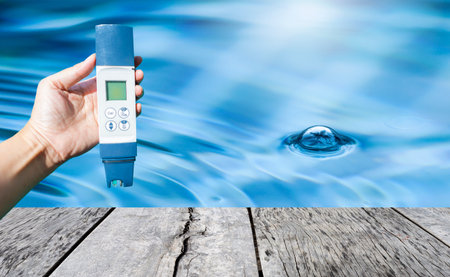 Swimming digital pool water testing in girl hand over clear pool water background, quality water tester technologyの写真素材