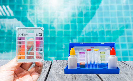 Mini tester in girl hand with water tester test kit on wooden table with space on clear swimming pool water background, quality water testing test kit, pool maintenance and serviceの写真素材