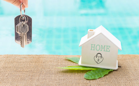 House key in girl hand with wooden house model on swimming pool edge, Green house, environmental concept, eco houseの写真素材