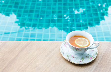 Hot tea with lemon slice in flower tea cup on swimming pool edge, hot drink, healthy drink