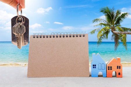 House key in girl hand with Miniature house and calendar over tropical beach background, property and real estate business conceptの写真素材