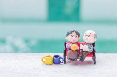 Miniature old couple on red bench with ceramic cup over blurred background, happy old coupleの写真素材