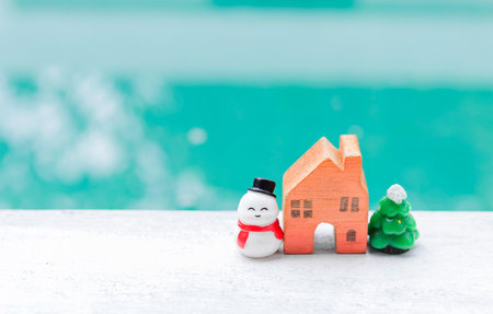 Snowman with orange house model and Christmas tree over blurred background, Christmas card background ideaの写真素材