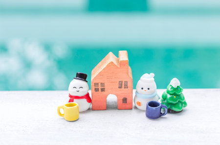 Miniature snowman with wooden house model and ceramic cup over blurred background, Christmas background idea, outdoor day lightの写真素材