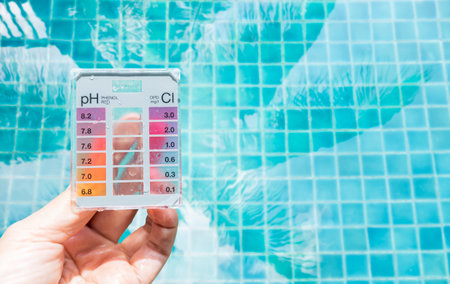 Swimming pool water tester test kit in girl hand over blurred swimming pool water background, quality water testing test kit, pool maintenance and service business conceptの写真素材