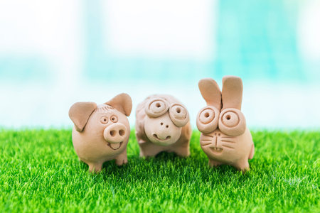 Cute little animal clay sculpture on artificial grass over blurred background, pig and rabbit for garden decorationの写真素材