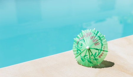 Green paper umbrella on swimming pool edge, summer season background