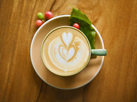 Hot coffee latte art heart shape  foam on wooden background.fersh coffee seeds and leaf on wood...