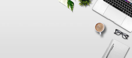 Top view of white office desk table with laptop, coffee cup, notebook, glasses and plant.