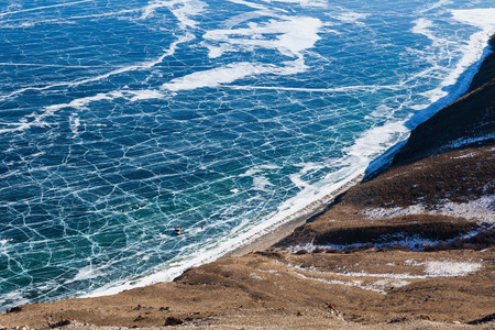 View of frozen Baikal lake from above in winter,with cracks on surface and fishermen drilling a hole,Russia.の写真素材