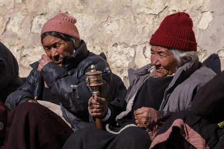 Leh,India-Feb 9,2013; Old female buddhist devotee is watching the mask dance,religious ceremony and swirl her prayer wheel at the ancient monastery in Ladakh,Jammu and Kashmirのeditorial素材