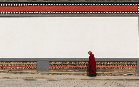 Xining,China-May 5,2014;Old male lama walk in front of traditional brick wall in the ancient monastery のeditorial素材