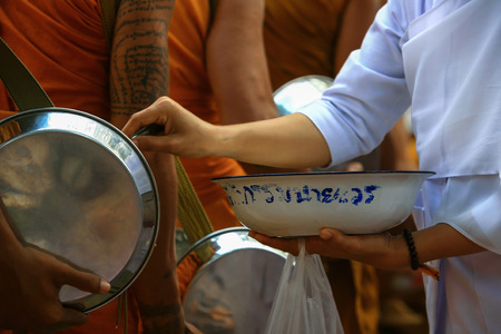 Food offering by buddhist Thai female in white dress to the monk.This ritual is a merit to spirit and others as Thai letters on the bowl mean "persons with previous deeds on each other"のeditorial素材