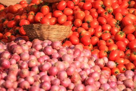 Pile of fresh organic red tomato with onion in foreground and bamboo wickerwork basketの写真素材