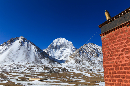 Beautiful scenery North face of sacred Kailash mountain covered with snow with old red brick building with golden tibetan umbrella on top in foreground and clear blue sky in background,Chinaの写真素材