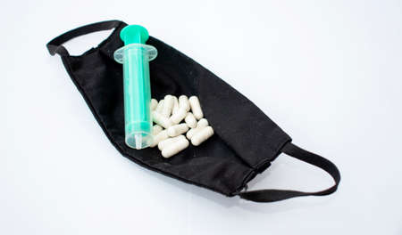 Many pills and a green syringe inside a black, fabric face mask on a white backgroundの写真素材