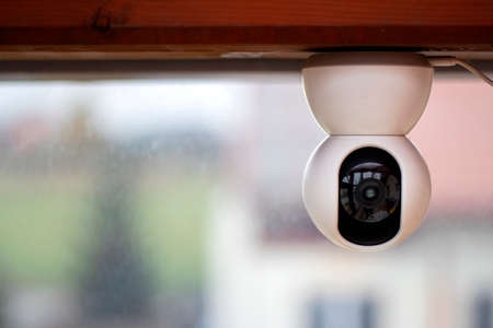 White CCTV camera mounted upside down on a wooden beam. The camera has a USB cable plugged into it and cleary visible lens.の写真素材