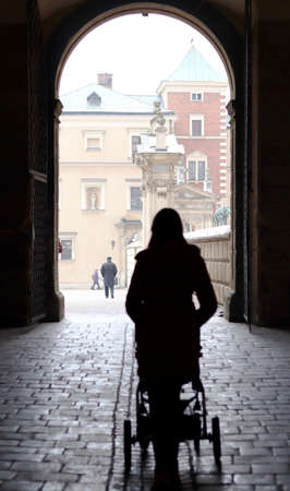 Silhouette of a woman pushing a stroller towards a gate on Wawel Castle hill in Poland, Krakowの写真素材