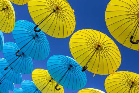 blue and yellow umbrellas hovering in the airの写真素材
