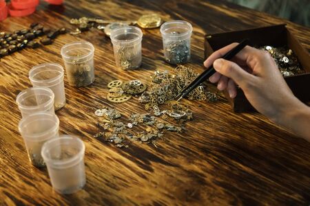 Girl sorts gears. The craftsman creates jewelry. Handmade with tweezers and cogwheels. Work with...