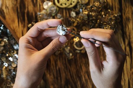 Girl craftsman dismantles clock shoot close up. Female hands holding tweezers. Repairing vintage...