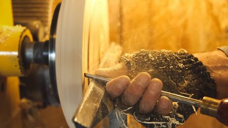 Woodworker cuts wood by gouge. Carpenter handles wood by machine. Builder works with workpiece in workspace. Making beautiful wooden handmade plate. Sawdust fly from detail in soft focus.の写真素材