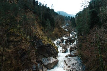 Small cliffy mountain spring waterfall in Abkhazia. Craggy ridge cliff with water bursts. Rocky mountains and waterfall rounded by trees. Rock mountains falling stream.の写真素材