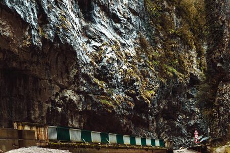 Bridge over the mountain river. Stone bag Abkhazia in spring. Canyon road surrounded by rocks.Trees grow on a ridge. Cliffy hills above the road. Unusual place in mountainous areas.の写真素材