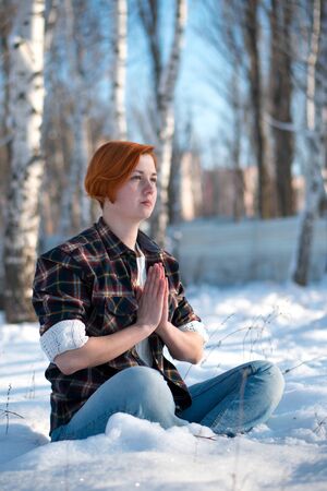 Girl resting in snowy forest in yoga pose. Beautiful young woman sitting in yoga position. Winter meditation concept.の写真素材