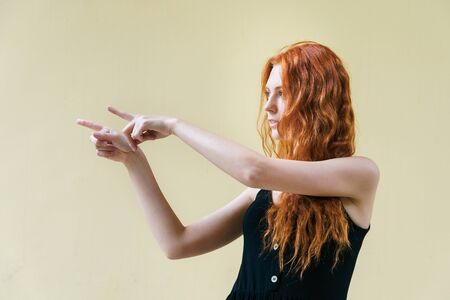 Young lady standing on yellow background. Ginger woman pointing fingers to the side.の写真素材