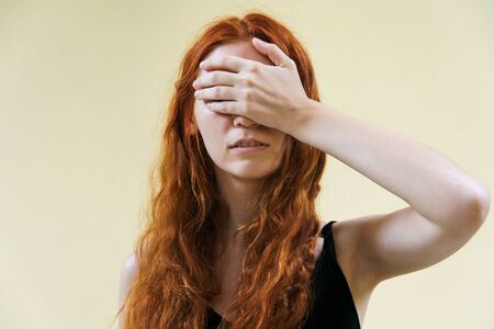 Young ginger woman closed her eyes by hand on yellow background.の写真素材