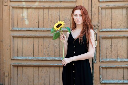 Girl with sunflower in hand on background of old wooden door. Simplicity and sincerity concept.の写真素材