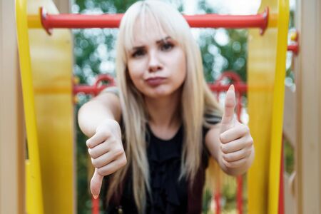 Beautiful blonde girl with blurred face shows thumbs up and down. Problem of choice concept. Like and dislike sign.の写真素材