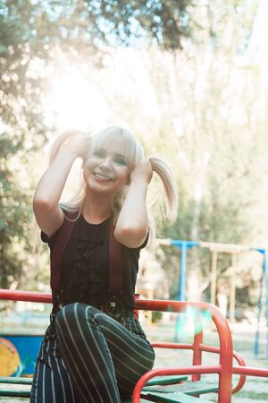 Beautiful blond girl with long hair on playground with blurred background, sun flare in frame.の写真素材