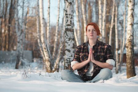 Girl in winter forest in lotus pose. Adherent of doctrine of yoga in frosty weather. Tranquility and concentration concept with copy space.の写真素材
