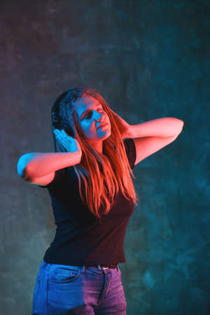 Girl with dreadlocks with multicolored neon lighting on dark background. Stylish young woman with headphones in futuristic environment. Night party concept with copy space.の写真素材