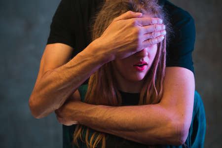 Man hides girl eyes by hand. Portrait of pair with colorful light on dark background, close up.の写真素材