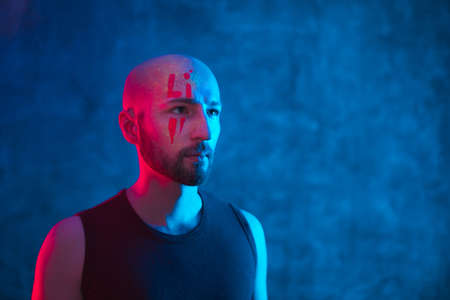 Portrait of beautiful bald-headed man with fluorescent makeup on face in ultraviolet and neon light looks on space for text. Art and sensuality concept.の写真素材