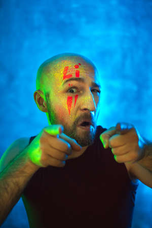 Stylish bald man points fingers at camera. Fluorescent paint in neon light. Way to meet in nightclub.の写真素材