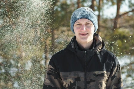Portrait of happy man surrounded by snowflakes enjoying cold and snowy time in winter forest, copy...