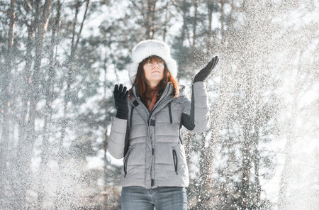 Joyful woman throws snow in frosty park. Sunny day outdoor. Winter vacation and joyful concept.