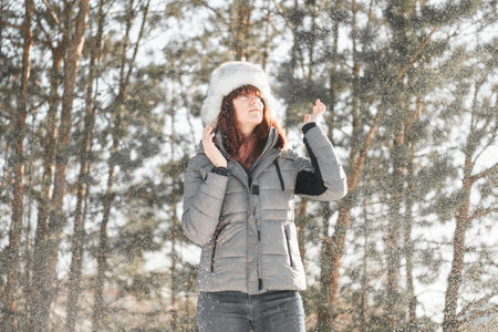 Winter fun. Woman plays throwing snow with arms up open in freedom enjoying cold season. Happy and...