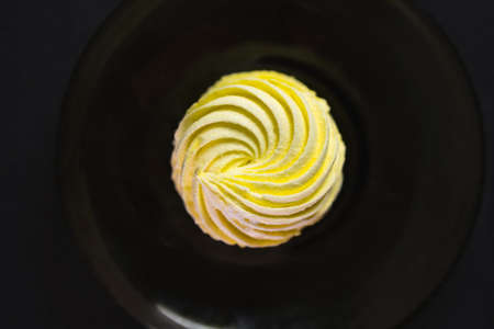 Yellow marshmallow on dark plate with black background. Food harmful to diabetics. Sweet addiction concept.の写真素材